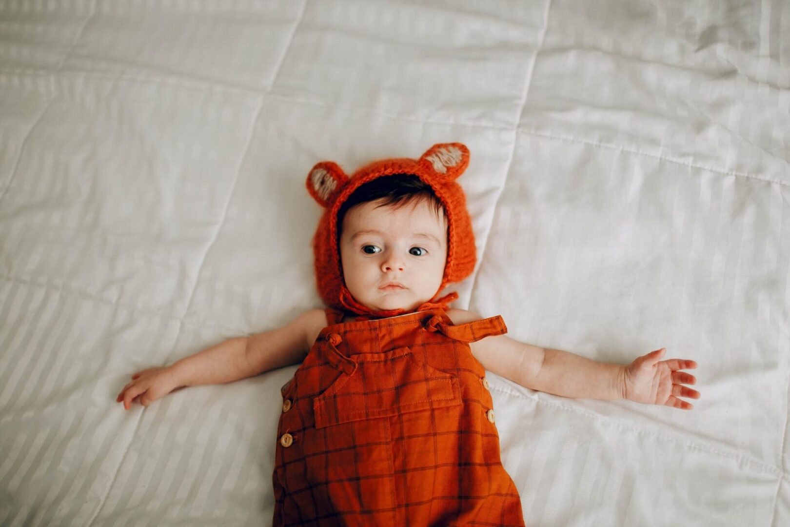 A baby in an orange outfit laying on the bed.