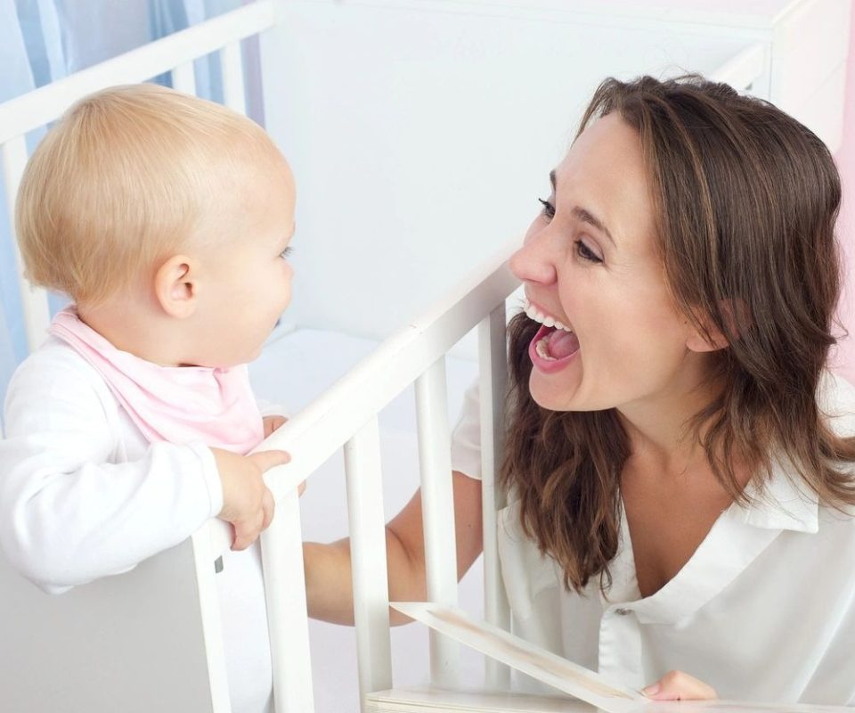 A woman is playing with her baby in the crib